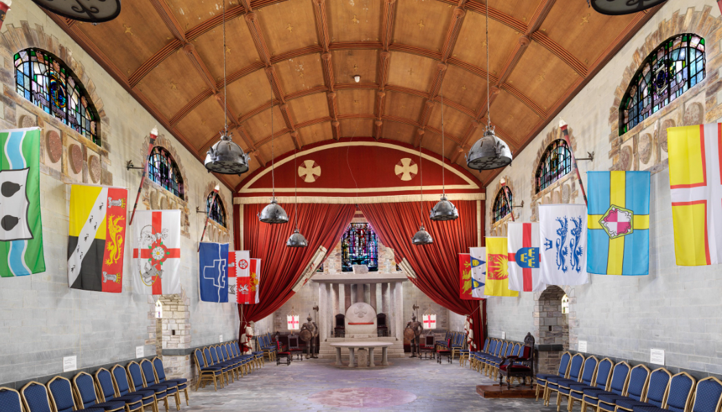 A photograph on the interior of a historic hall with a arched wooden roof at colourful flags adorning the walls